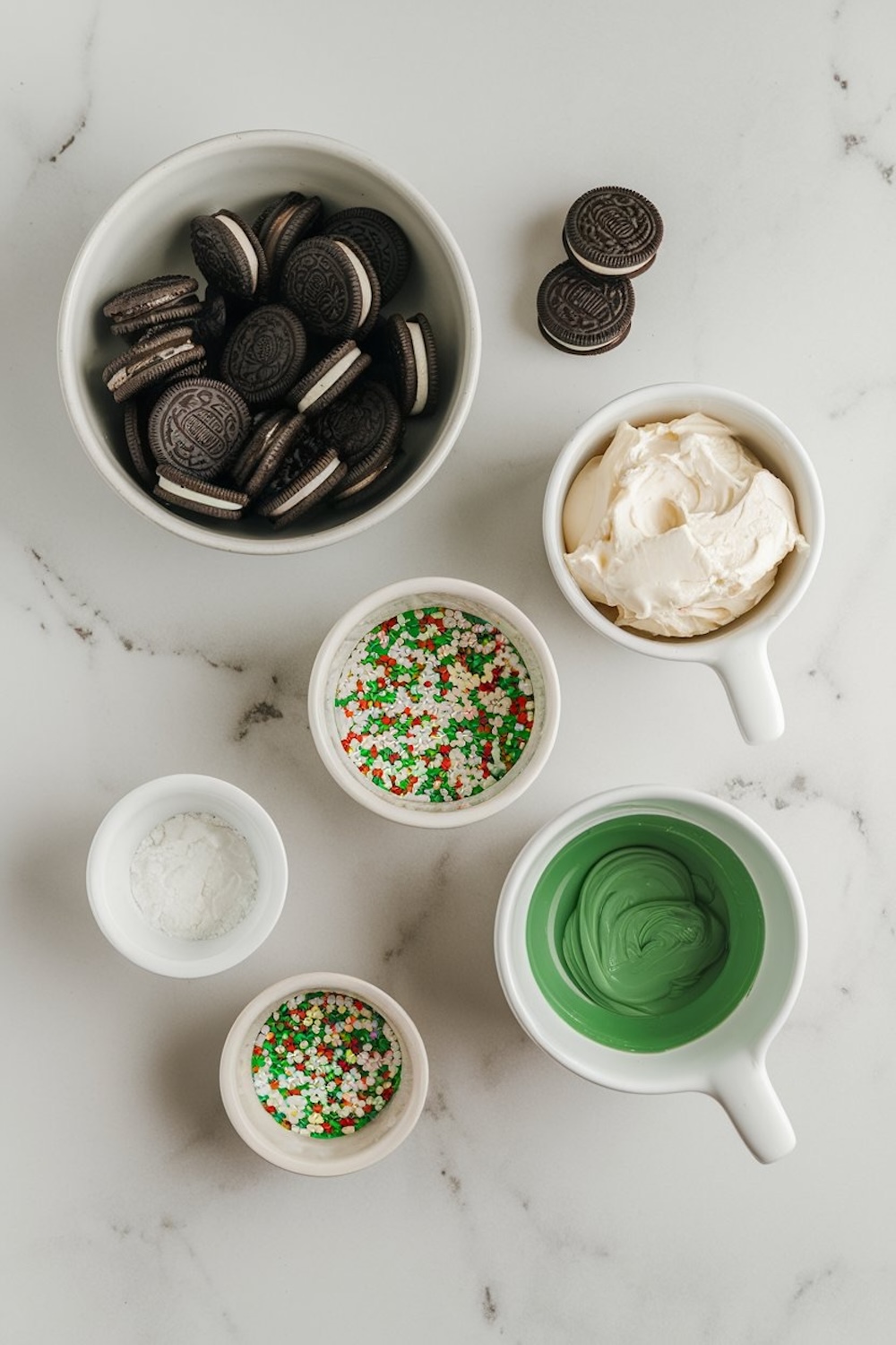 Overhead shot of key ingredients needed for Irish Cream Oreo truffles, arranged on a marble surface. The setup includes Oreo cookies, green chocolate coating, cream cheese, and colorful sprinkles, providing a clear and organized view for easy recipe preparation.
