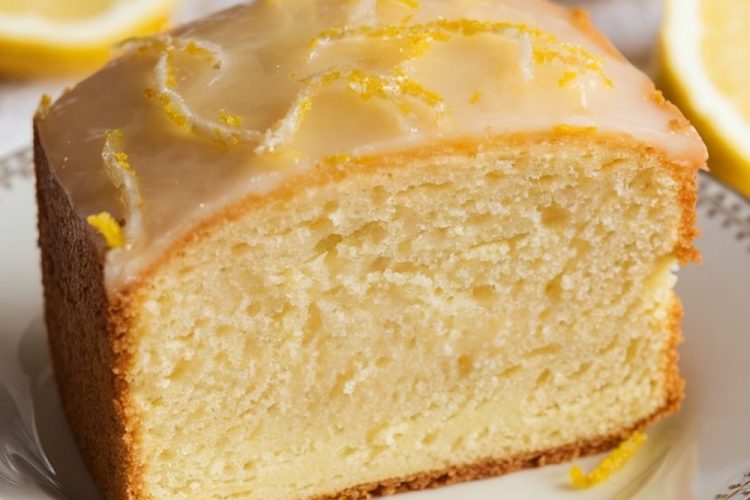 A single slice of lemon pound cake with a tender crumb and shiny lemon glaze, garnished with lemon zest, served on a delicate china plate. The slice reveals the cake's moist, buttery texture, ideal for showcasing a classic dessert with a refreshing citrus twist.