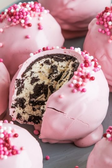 Close-up of an Oreo truffle ball cut in half, highlighting the creamy, Oreo-filled center and pink candy shell topped with pink, white, and red sprinkles. Perfect for romantic or festive occasions. Keywords: Oreo truffle close-up, pink sprinkle toppings, festive dessert ideas, Oreo and cream cheese filling, eye-catching desserts.