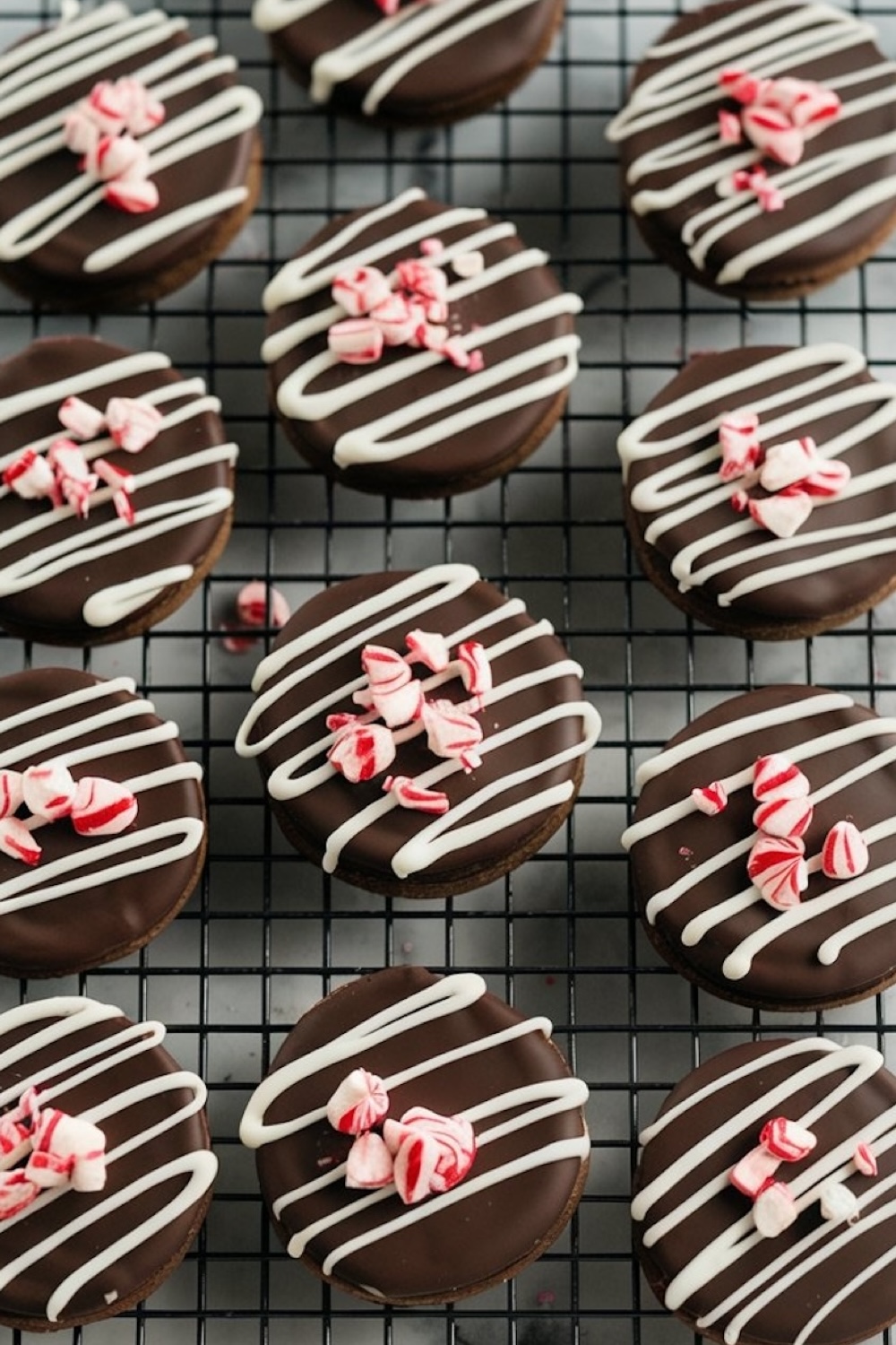Fully decorated peppermint bark cookies on a wire rack, each cookie adorned with white chocolate drizzle and sprinkled with vibrant red and white peppermint pieces for a festive holiday look.