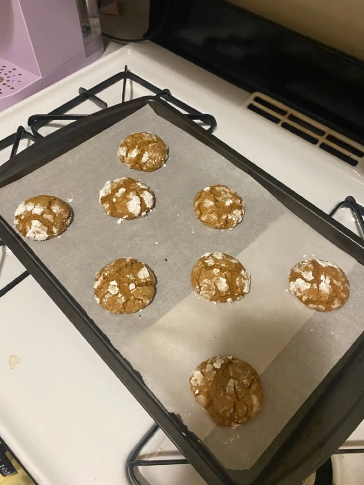 Eight gingerbread crinkle cookies spaced evenly on white parchment paper. Baked to a soft golden brown with cracked sugar tops, showing even round shape and lightly crisped edges.
