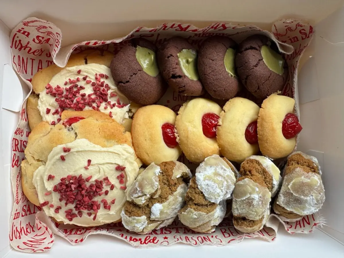 Holiday cookie gift box featuring gingerbread crinkle cookies with white chocolate, cherry thumbprints, and frosted sugar cookies. Packed in festive red-and-white paper, ready for Christmas gifting.
