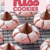 Strawberry Kiss cookies cooling on a wire rack. The soft, pink cookies are topped with chocolate Hershey’s Kisses and sprinkled lightly with powdered sugar, showcasing their cracked, delicate texture. Ideal for a Pinterest-worthy holiday baking project.
