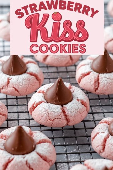 Strawberry Kiss cookies cooling on a wire rack. The soft, pink cookies are topped with chocolate Hershey’s Kisses and sprinkled lightly with powdered sugar, showcasing their cracked, delicate texture. Ideal for a Pinterest-worthy holiday baking project.
