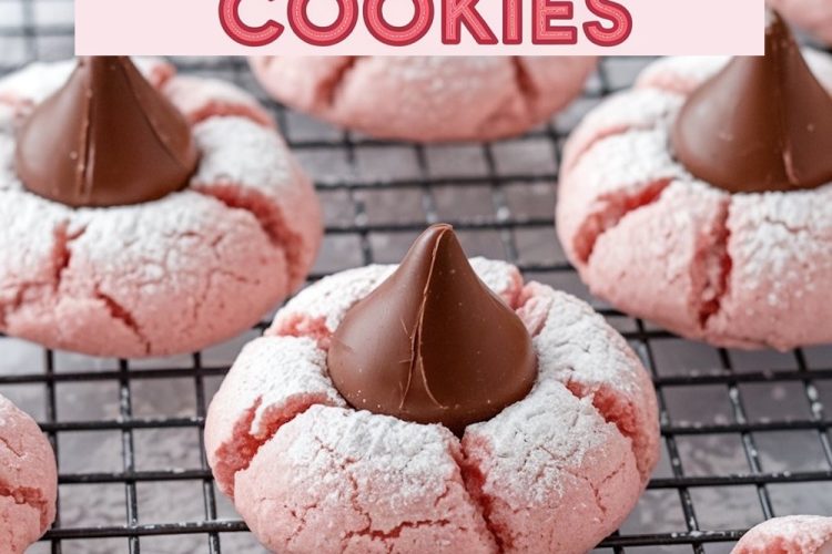 Strawberry Kiss cookies cooling on a wire rack. The soft, pink cookies are topped with chocolate Hershey’s Kisses and sprinkled lightly with powdered sugar, showcasing their cracked, delicate texture. Ideal for a Pinterest-worthy holiday baking project.