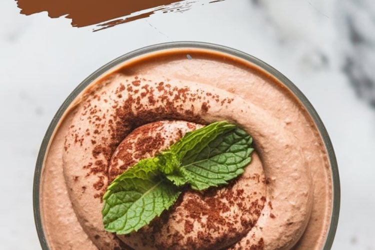 A single serving of avocado chocolate mousse dusted with cocoa powder and garnished with fresh mint leaves. The dessert sits in a glass, with text overlay reading “Avocado Chocolate Mousse” in bold, brushstroke-style font.