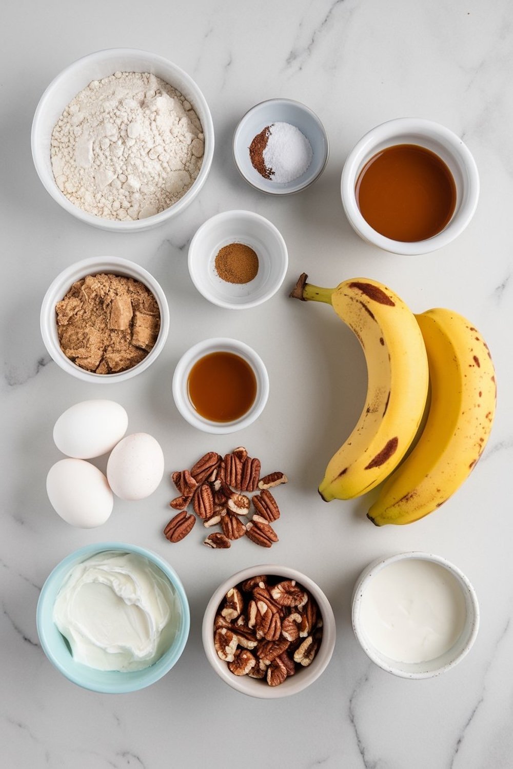 Flat-lay of the ingredients for caramel pecan banana bread arranged neatly on a white surface. Items include bananas, flour, brown sugar, eggs, pecans, vanilla extract, yogurt, and spices like cinnamon and nutmeg.