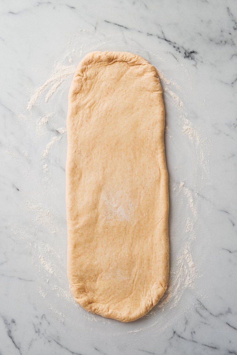 A rectangle of rolled-out croissant dough dusted with flour on a marble surface, ready for shaping and layering.