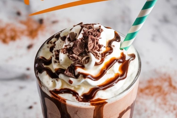 A creamy chocolate milkshake served in a tall glass, topped with whipped cream, chocolate shavings, and a drizzle of chocolate syrup. A green and white striped straw is placed in the milkshake. The background features cocoa powder and chocolate syrup splatters.