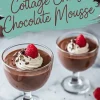 Two glasses of cottage cheese chocolate mousse garnished with whipped cream, a raspberry, and chocolate shavings, with one raspberry placed on the countertop and the text overlay “Cottage Cheese Chocolate Mousse.”