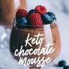 Close-up of keto chocolate mousse in a glass, garnished with fresh raspberries and blueberries. The text overlay reads “Keto Chocolate Mousse,” with blurred berries in the background adding depth to the composition.