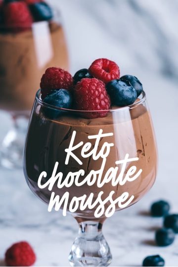 Close-up of keto chocolate mousse in a glass, garnished with fresh raspberries and blueberries. The text overlay reads “Keto Chocolate Mousse,” with blurred berries in the background adding depth to the composition.