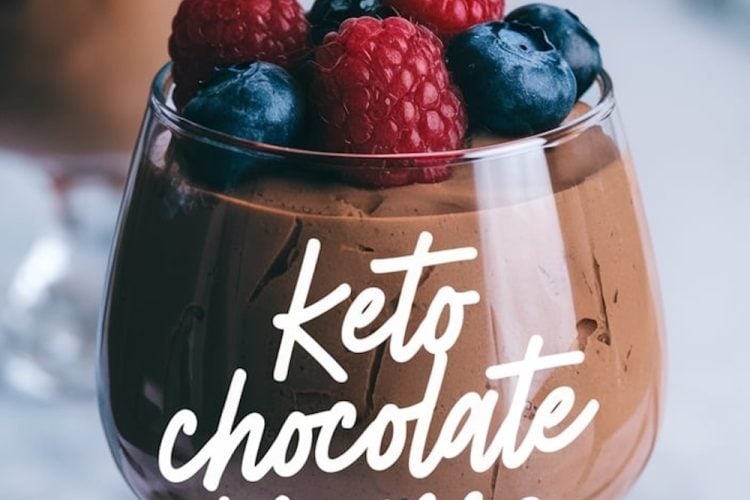 Close-up of keto chocolate mousse in a glass, garnished with fresh raspberries and blueberries. The text overlay reads “Keto Chocolate Mousse,” with blurred berries in the background adding depth to the composition.
