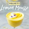 A glass of lemon mousse topped with whipped cream, a lemon slice, and small purple flowers, with the text “Velvety Lemon Mousse” overlaid on the image.