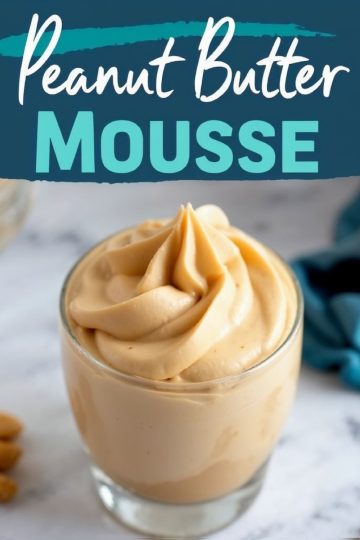 A glass of creamy peanut butter mousse with a swirled, fluffy texture. The dessert sits on a marble surface with text overlay reading “Peanut Butter Mousse” in bold, colorful font. A blue napkin and peanuts are visible in the background.