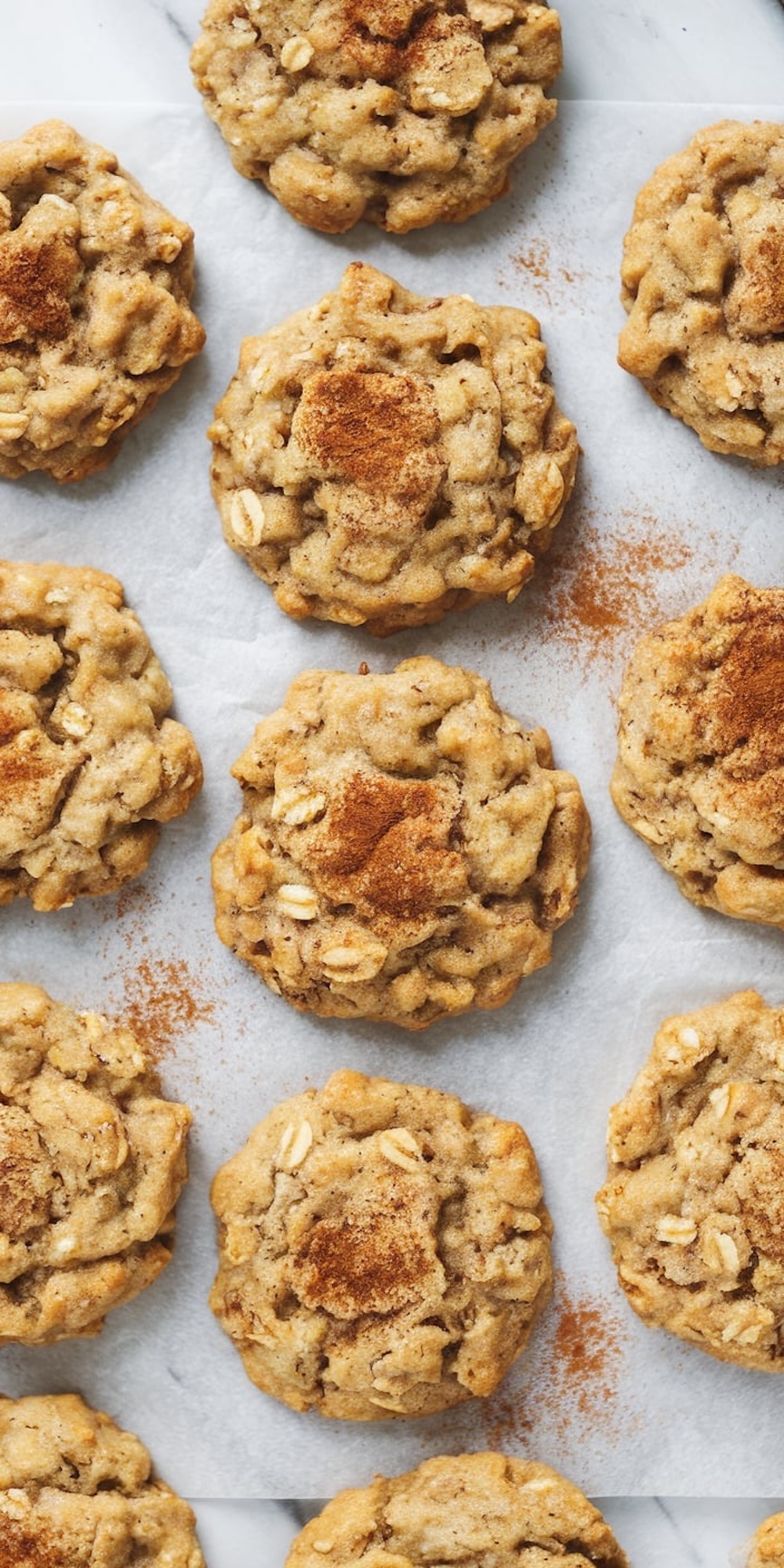 Close-up of freshly baked spiced banana oatmeal cookies arranged on parchment paper. The cookies are golden brown, sprinkled with cinnamon, and feature a chewy, textured appearance.
