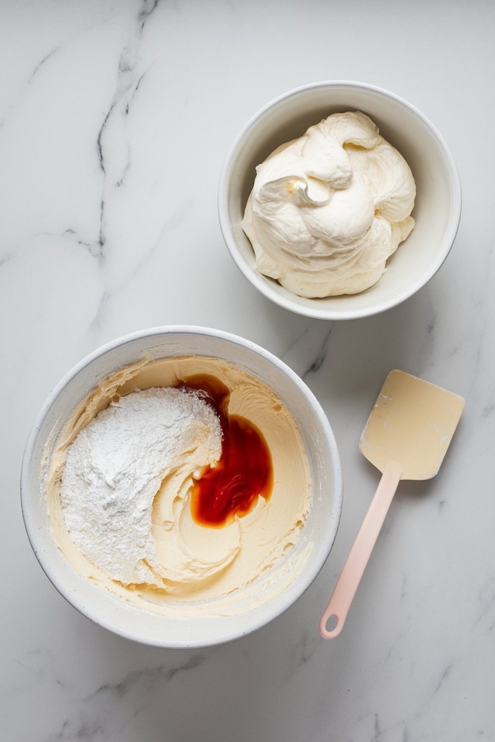 A mixing bowl with whipped mascarpone cream and powdered sugar blended with vanilla extract, paired with another bowl of smooth, fluffy whipped cream on a white marble surface.