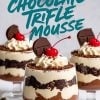 A trio of decadent triple chocolate mousse trifles served in glass cups, layered with chocolate mousse, whipped cream, and chocolate shavings. Each is topped with whipped cream, a chocolate square, and a maraschino cherry. Text overlay reads “Triple Chocolate Trifle Mousse” in bold turquoise lettering.