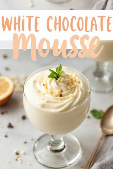 Close-up of a glass of creamy white chocolate mousse, garnished with a sprig of fresh mint and sprinkled with white chocolate bits. The text overlay reads “White Chocolate Mousse” in soft peach tones. Background elements include a slice of lemon, scattered chocolate chips, and a golden spoon, enhancing the refined setting.