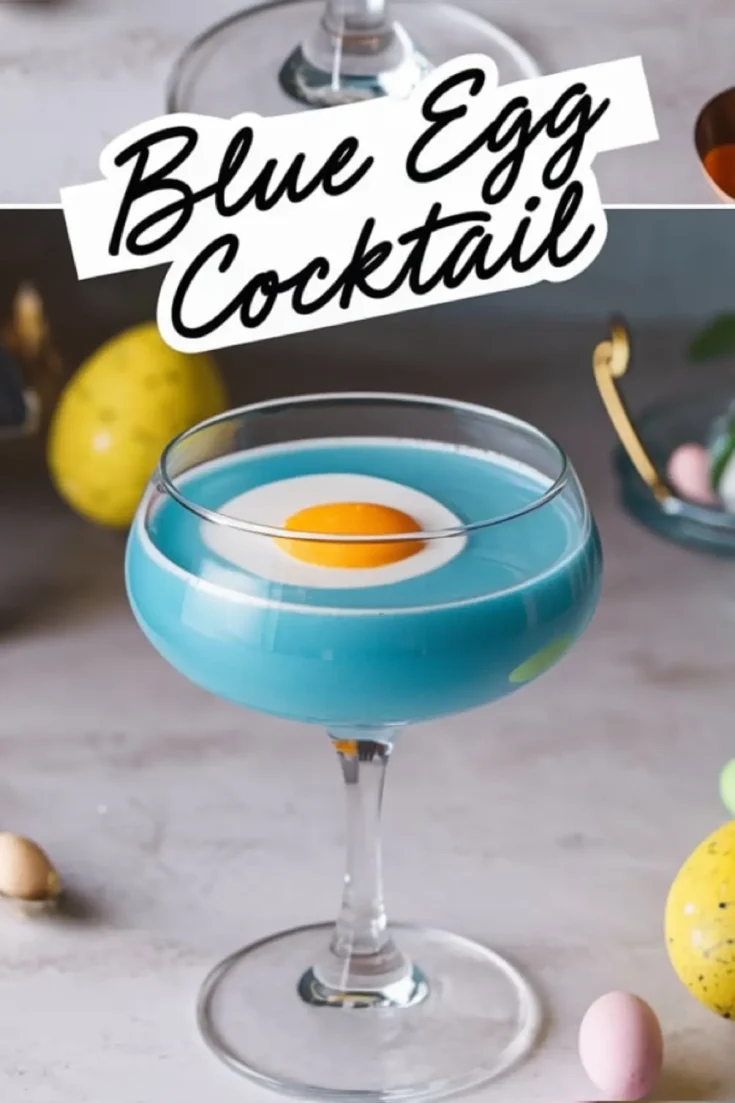 Close-up of a blue egg cocktail in a coupe glass with a white layer and an apricot garnish resembling a fried egg. The elegant glass is surrounded by pastel Easter eggs and festive decorations, emphasizing a fun and creative Easter-inspired drink presentation.