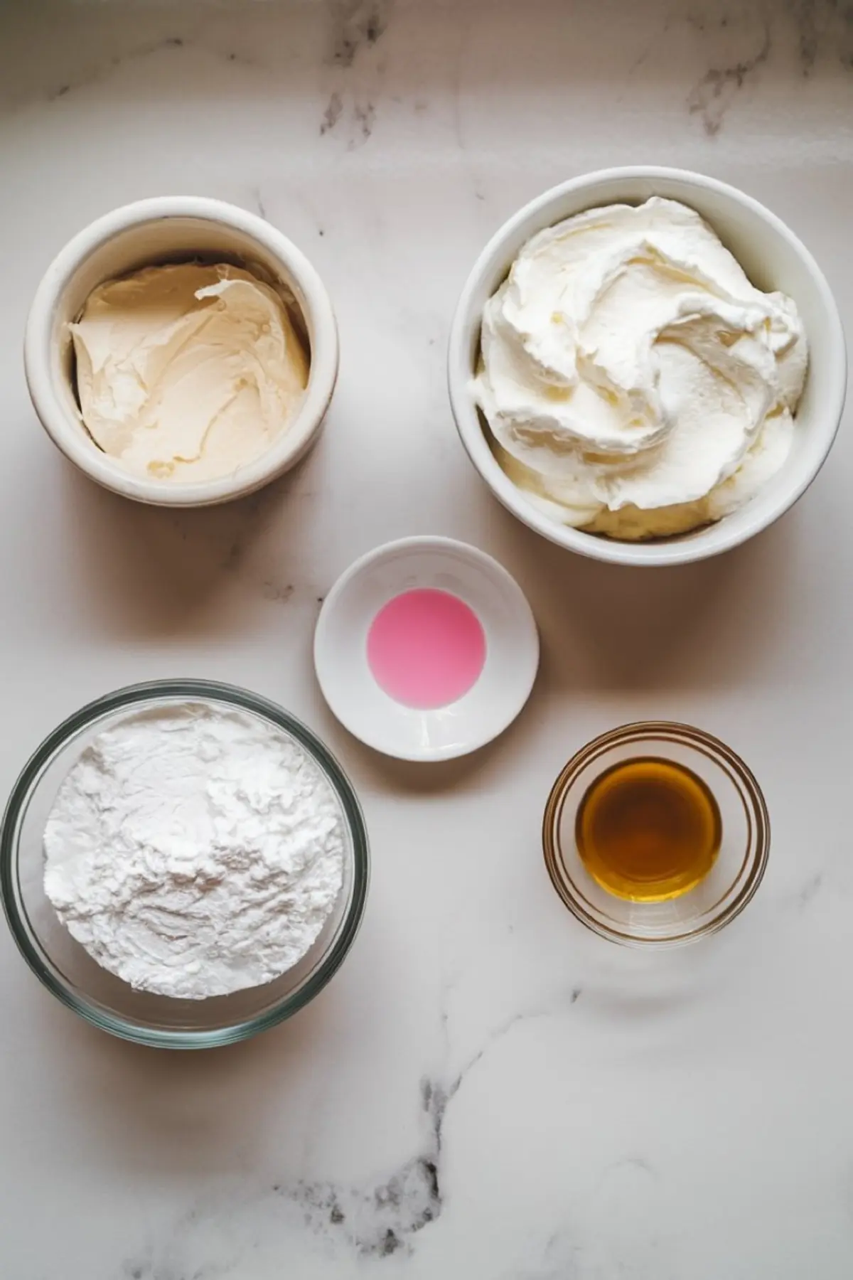 A flat lay of Easter dip ingredients arranged on a marble surface, including cream cheese, whipped topping, powdered sugar, vanilla extract, and pink food coloring.
