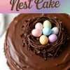 A close-up of an Easter egg nest cake with smooth chocolate ganache coating. A decorative chocolate nest on top holds pastel candy eggs. The background features a colorful gradient with the text “Easter Egg Nest Cake.”