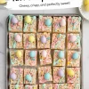 A baking tray filled with Easter-themed Rice Krispie Treats, each square topped with colorful pastel candy eggs, vibrant drizzle in pink, blue, and green, and festive sprinkles. Surrounding the tray are bowls of pastel candy eggs on a marble countertop, enhancing the playful holiday vibe.