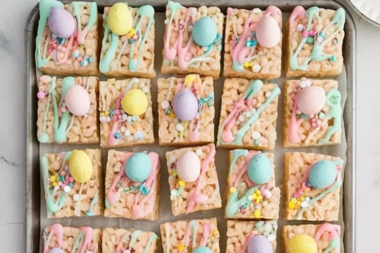 A baking tray filled with Easter-themed Rice Krispie Treats, each square topped with colorful pastel candy eggs, vibrant drizzle in pink, blue, and green, and festive sprinkles. Surrounding the tray are bowls of pastel candy eggs on a marble countertop, enhancing the playful holiday vibe.
