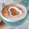 Close-up of blue Easter Egg-Hunt martinis in coupe glasses, topped with a frothy white foam and cocoa powder shaped like an egg. The vibrant blue color contrasts with the white foam, creating a festive and playful presentation.