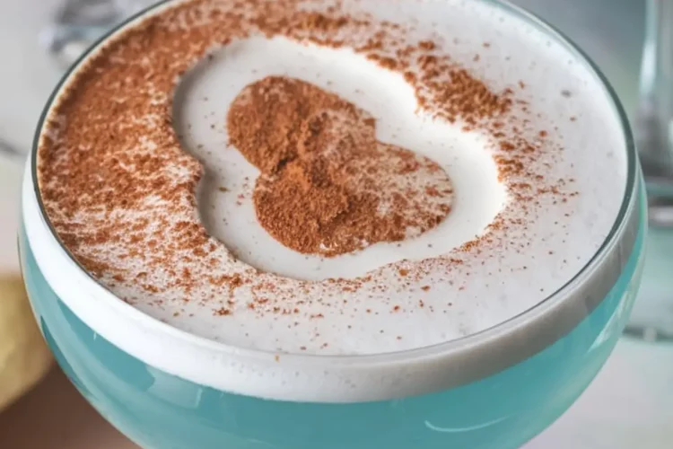 Close-up of blue Easter Egg-Hunt martinis in coupe glasses, topped with a frothy white foam and cocoa powder shaped like an egg. The vibrant blue color contrasts with the white foam, creating a festive and playful presentation.