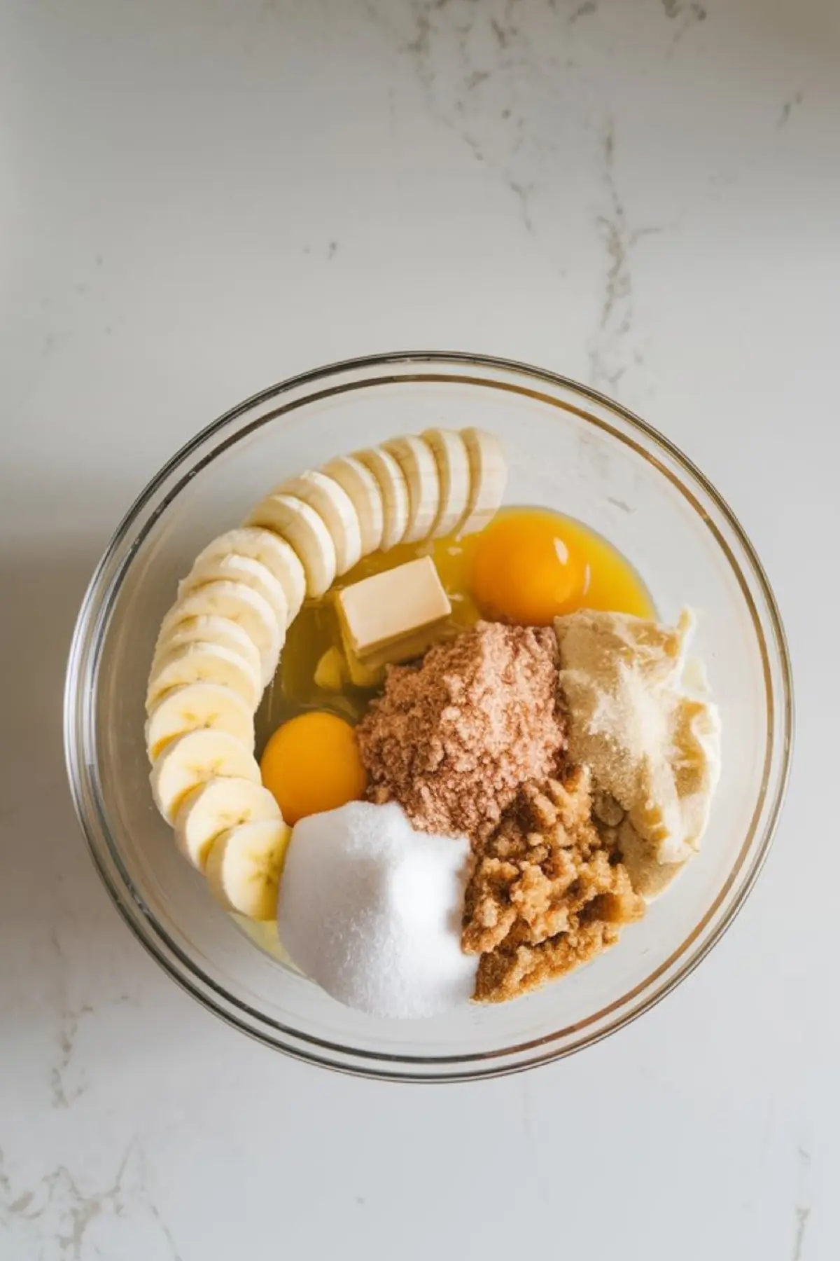 Mixing bowl filled with banana bread ingredients, including sliced bananas, eggs, brown sugar, white sugar, butter, and spices, ready to be blended.