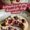 A close-up of freshly baked maraschino cherry chocolate chip cookies on a decorative plate. One cookie has a bite taken out, showing the gooey chocolate and juicy cherries inside. A text overlay in cursive font reads “maraschino cherry chocolate chip cookies.”