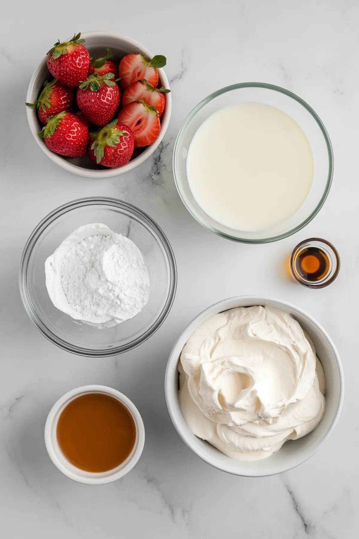 Ingredients for Twinkies cake on a marble countertop, including fresh strawberries, heavy cream, powdered sugar, whipped topping, caramel sauce, and vanilla extract, arranged in glass and ceramic bowls.