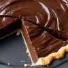 Close-up of a chocolate pie with a slice removed, showing the thick, glossy chocolate filling with a smooth swirl pattern in a baked pie crust.
