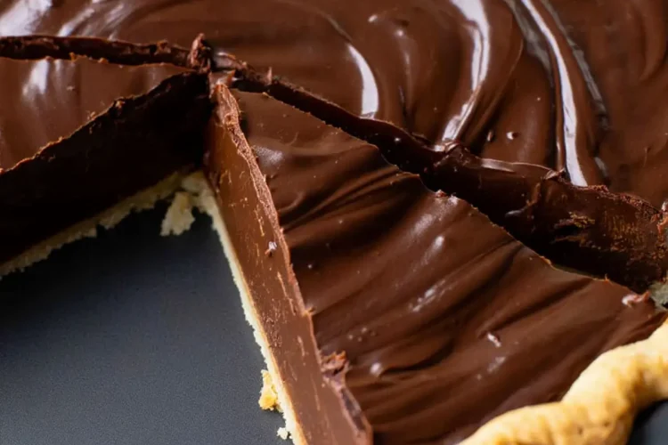 Close-up of a chocolate pie with a slice removed, showing the thick, glossy chocolate filling with a smooth swirl pattern in a baked pie crust.
