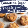 A baking tray with several cinnamon sugar French toast muffins, their tops slightly cracked and caramelized. The muffins are arranged casually with some slightly tilted. A bold, navy text overlay highlights the recipe title.