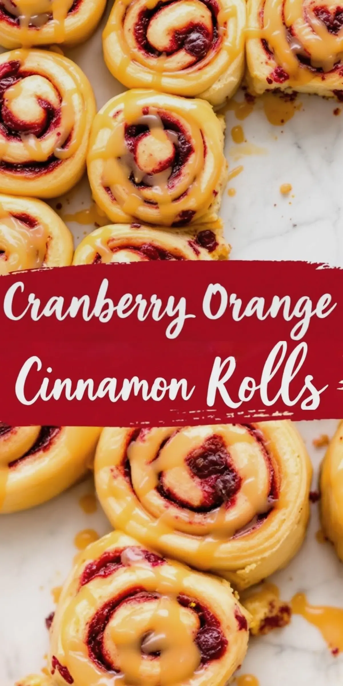 A close-up view of cranberry orange cinnamon rolls on a marble surface, topped with a smooth caramel glaze. The deep red cranberry filling contrasts with the soft, golden dough. A red banner with white lettering reads “Cranberry Orange Cinnamon Rolls.”