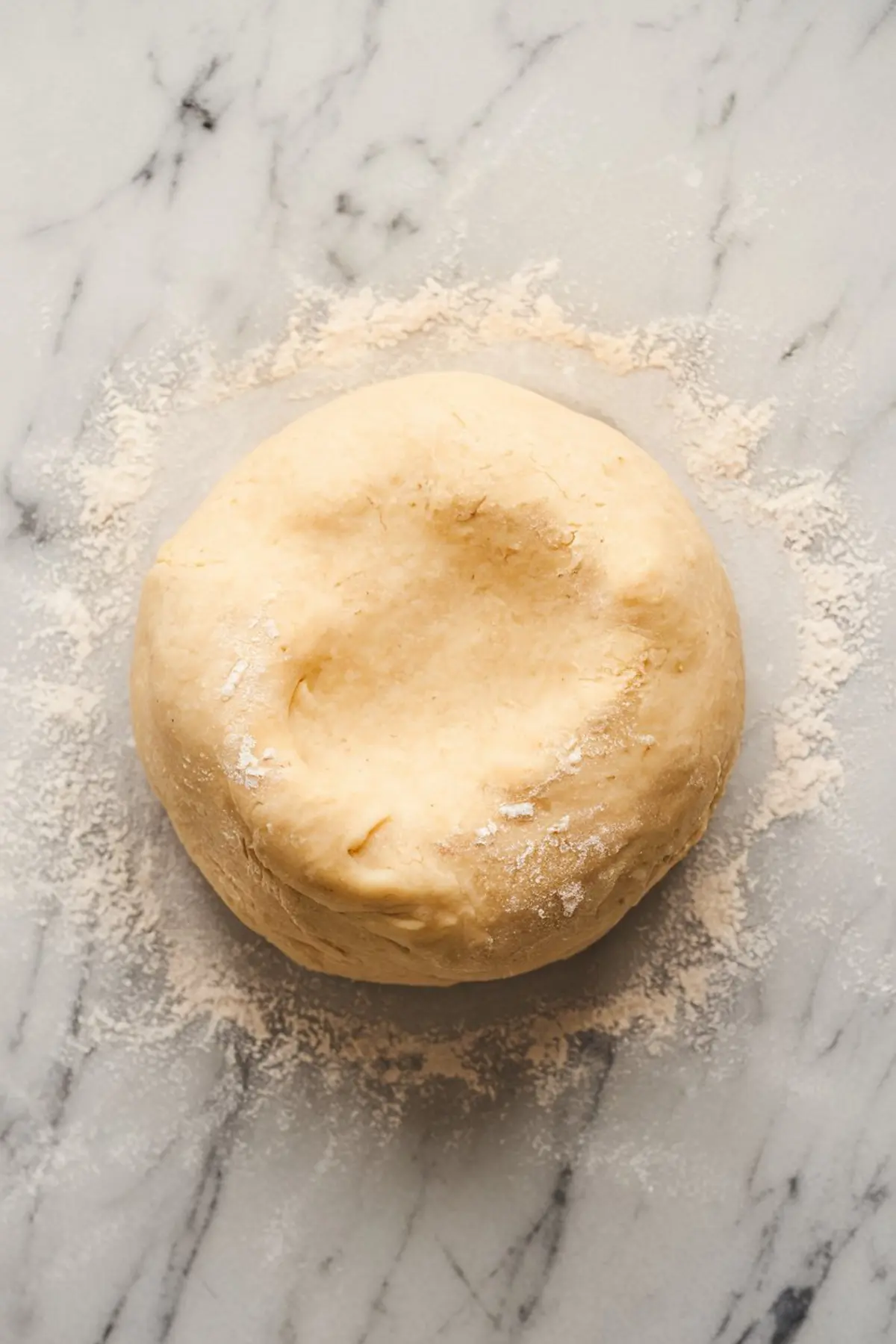 Close-up of a smooth, round ball of pie dough resting on a floured marble surface, prepared for rolling out into a pie crust.