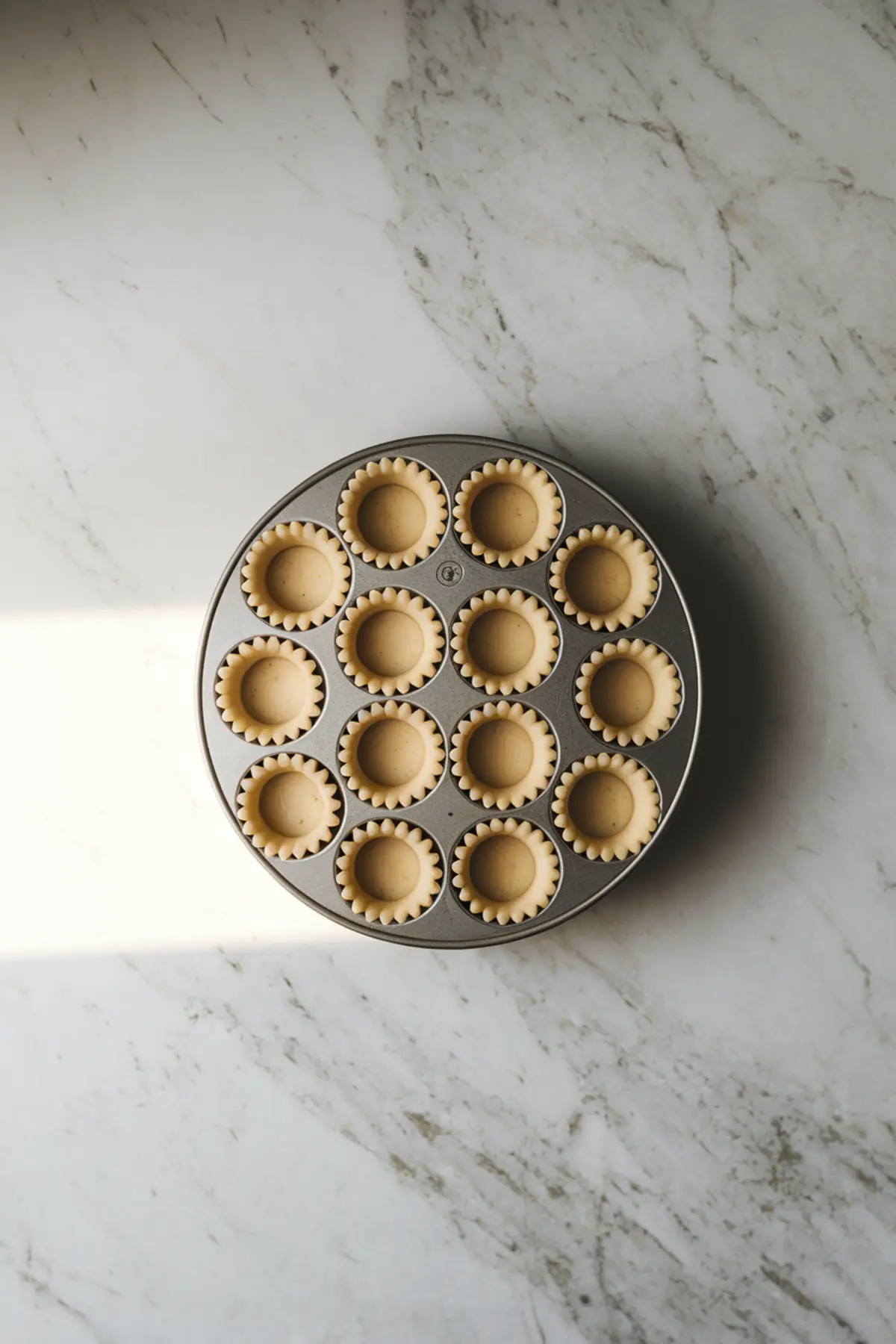 Overhead shot of a mini tart pan filled with unbaked pastry shells, neatly arranged on a marble surface, ready to be baked for lemon coconut tassies.