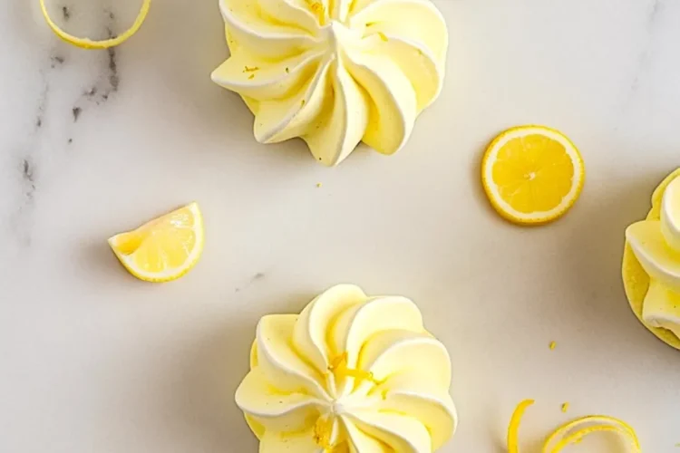 Overhead view of lemon meringue cookies swirled with yellow and white, surrounded by lemon zest curls and lemon slices, with “Lemon Meringues” text in bold purple over a yellow brushstroke banner.