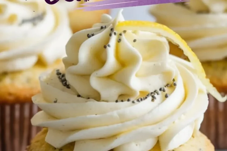 Close-up of a single lemon poppy seed cupcake with smooth buttercream frosting, poppy seeds, and a curled lemon zest garnish. The background features more cupcakes and a marble countertop.