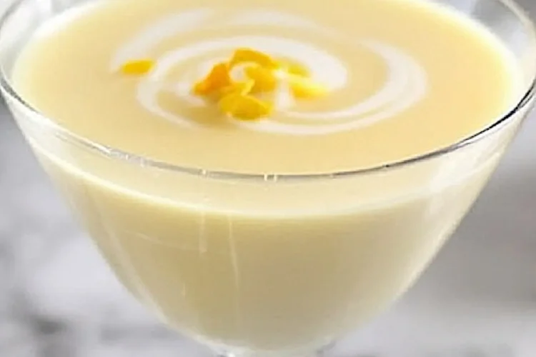 Close-up of a single lemon posset in a clear dessert glass with a swirl of cream and lemon zest topping, overlaid with the text “Lemon Possets Easy & Elegant.”