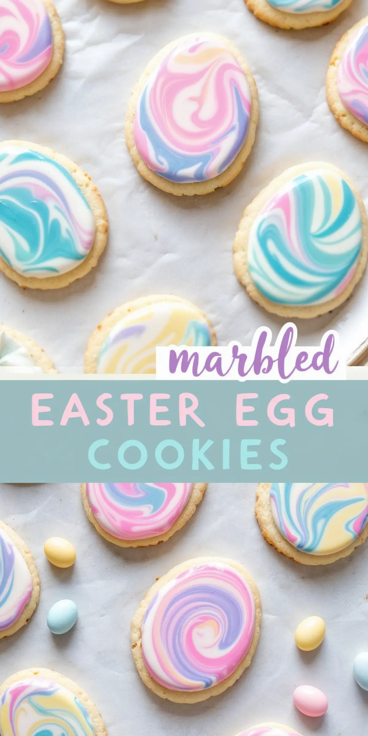 Marbled Easter egg cookies decorated with swirls of pastel pink, blue, yellow, and purple icing on an oval-shaped sugar cookie base, set on parchment paper with small candy eggs nearby. A festive Easter treat for kids.
