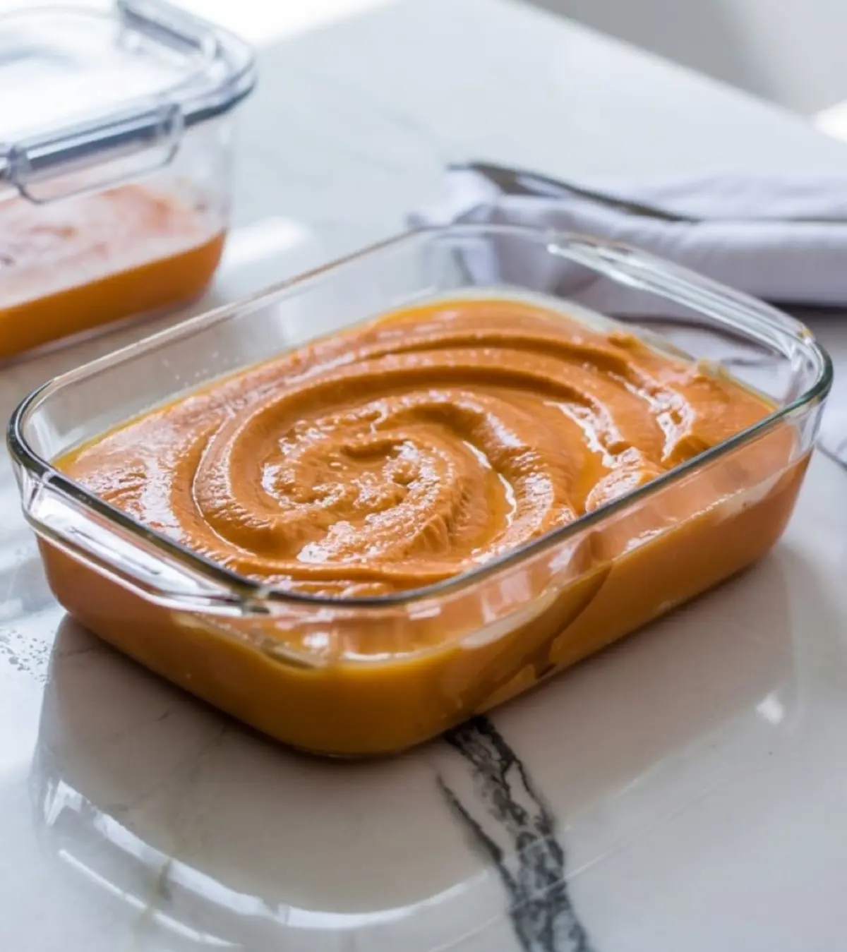 Glass dish filled with swirled cantaloupe puree set on a marble surface, ready to be frozen for granita preparation.
