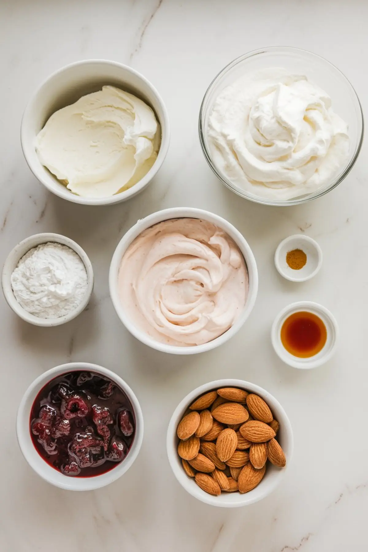 Flat lay of individual ingredients in small bowls for making cherry almond dip, including cream cheese, whipped cream, powdered sugar, cherry mixture, almonds, vanilla extract, and a pink whipped base.
