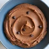 Smooth chocolate hummus swirled in a blue bowl, topped with scattered chocolate chips on a white marble background.