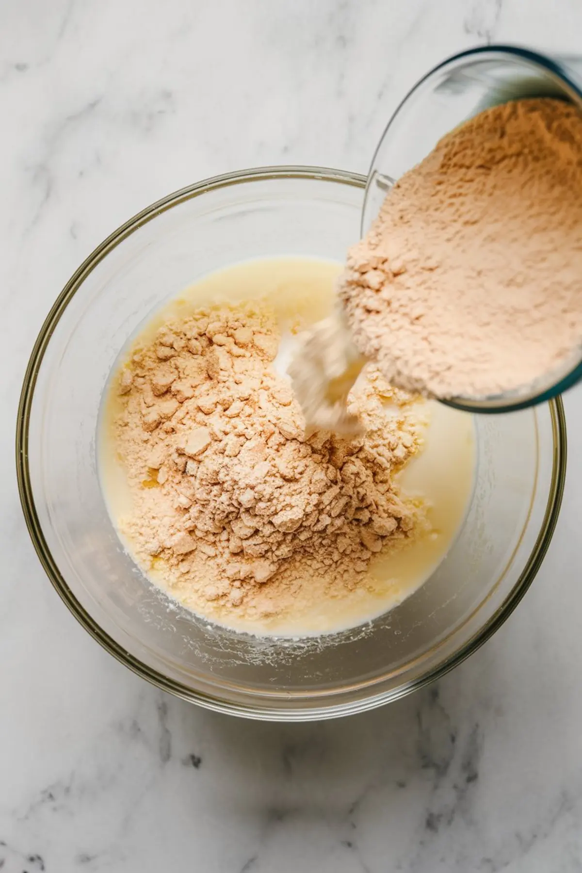 Action shot of dry pudding mix being poured into a bowl of sweetened condensed milk, showing the early step of mixing ingredients for banana pudding.