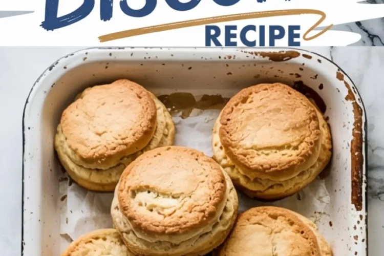 Golden brown biscuits stacked in a rustic white enamel baking tray, showcasing a fluffy, layered texture with a cracked top crust and a dusting of flour, set against a marble countertop.