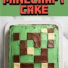 Top-down view of a Minecraft cake featuring bright green frosting and a pixelated pattern made from milk and white chocolate squares, set on a white plate against a marble background.
