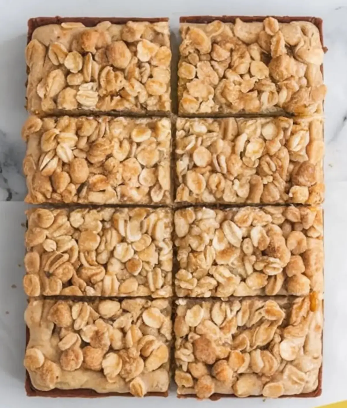 Golden oatmeal crumble bars cut into nine even squares on a marble surface, showcasing a textured topping of rolled oats and brown sugar.